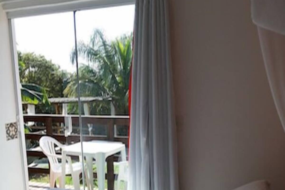 A hotel room with a bed, a view of the outdoor area, and a table and chairs outside.