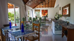 A spacious dining area with wooden tables and chairs, a kitchen area with a counter, and large windows providing natural light. - Pousada Caminho das Aroeiras (Búzios)