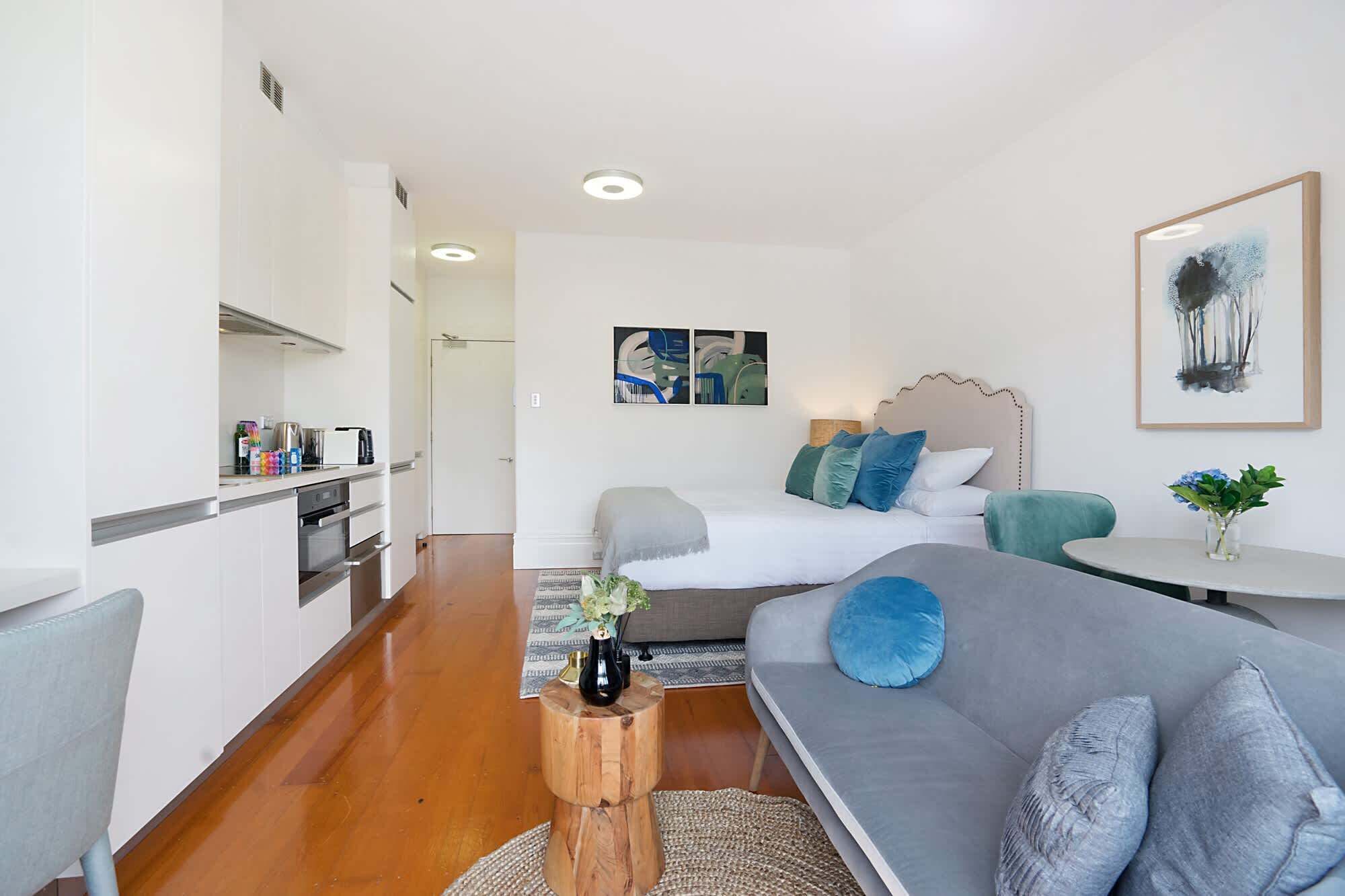 A modern, well-lit bedroom with a large bed, a grey sofa, and a small table with a vase.