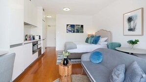 A modern, well-lit bedroom with a large bed, a grey sofa, and a small table with a vase. - Cozy Studio with Balcony in Unbeatable Location (Glebe)