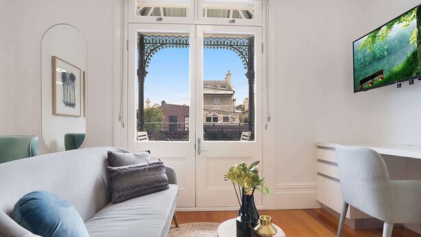 A modern living room with a sofa, a desk, and a TV. - Cozy Studio with Balcony in Unbeatable Location (Glebe)