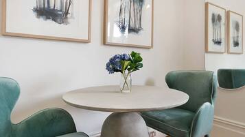A dining area with a round table, two teal chairs, and a vase with blue flowers.