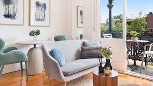 A modern living room with a sofa, chairs, a round table, and artwork on the walls. - Cozy Studio with Balcony in Unbeatable Location (Glebe)