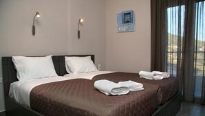 A double bed with brown and white bedding, two wall-mounted lights, and a framed 'LOVE' sign on the wall. - Akrotiri Panorama (Agios Vasileios)