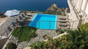 A rooftop pool with a clear view of the ocean, surrounded by rocks and greenery. - Akrotiri Panorama (Agios Vasileios)