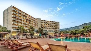 A hotel with multiple balconies, a swimming pool, and lounge chairs.