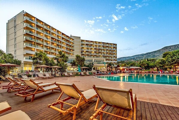 Un hotel con varios balcones, piscina y sillones de descanso.