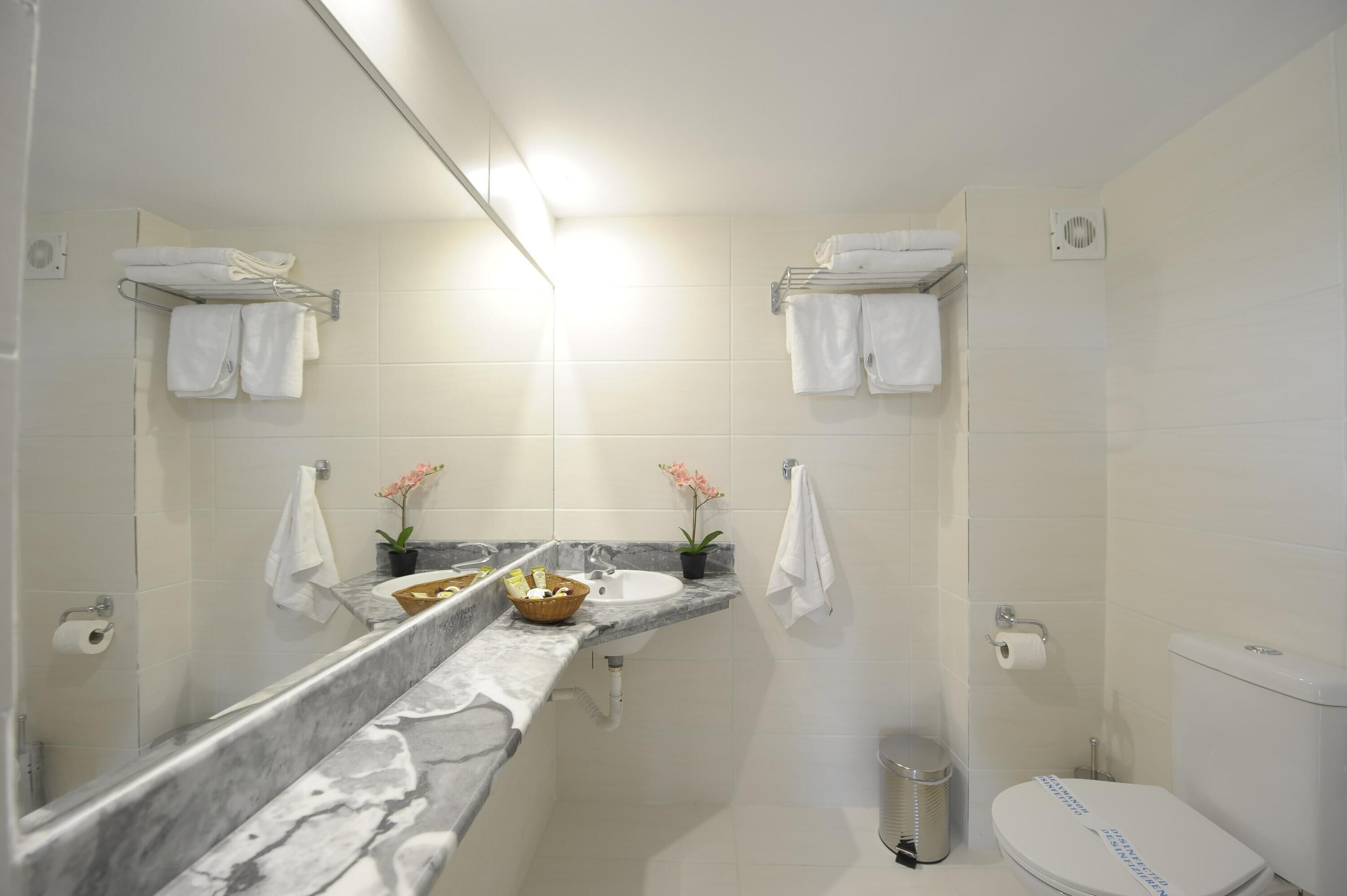 A modern bathroom with a marble countertop, two sinks, a toilet, and a trash can.