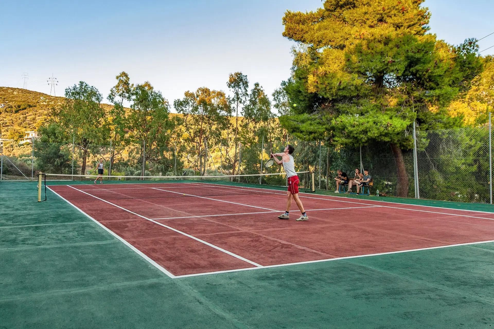 A tennis court with a net, surrounded by trees and a fence.