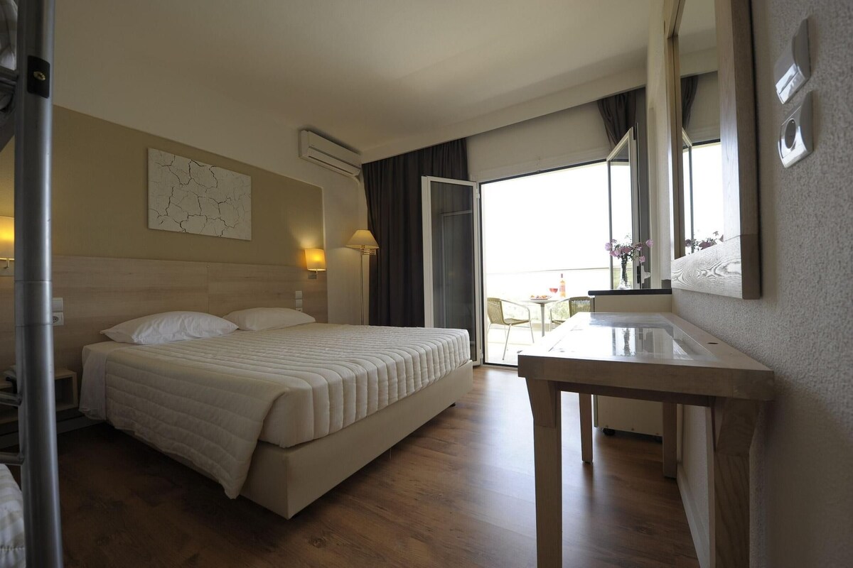 A hotel room with a bed, bedside table, and a view of the outdoors.