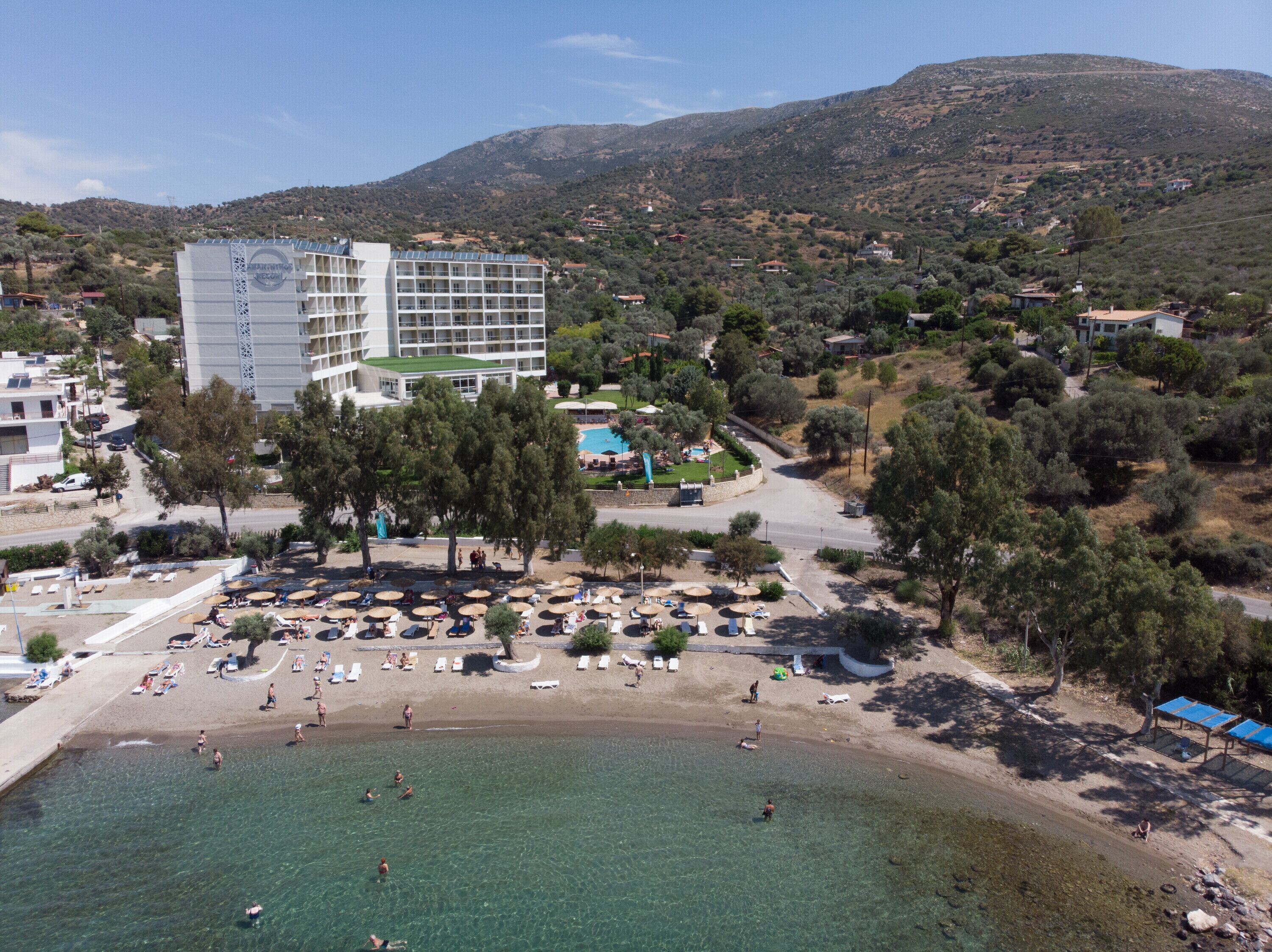 Hotel sul lungomare con piscina, spiaggia e montagne sullo sfondo.