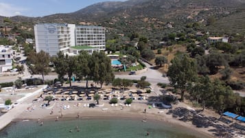 Hotel sul lungomare con piscina, spiaggia e montagne sullo sfondo.