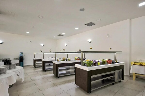 A clean, well-lit room with three buffet stations, a water dispenser, and a small seating area with a table and chairs.
