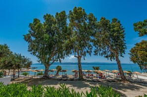 A beach with umbrellas, lounge chairs, and a clear view of the sea and distant mountains. - Evia Riviera Resort by Anayia All Inclusive Resorts (Eretria)
