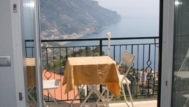 A balcony with a table and chairs, overlooking a coastal landscape. - Residenza Sveva (Ravello)