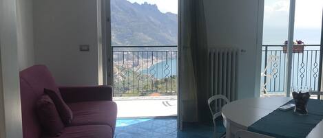A room with a pink sofa, a white table with chairs, and a view of mountains through large windows.