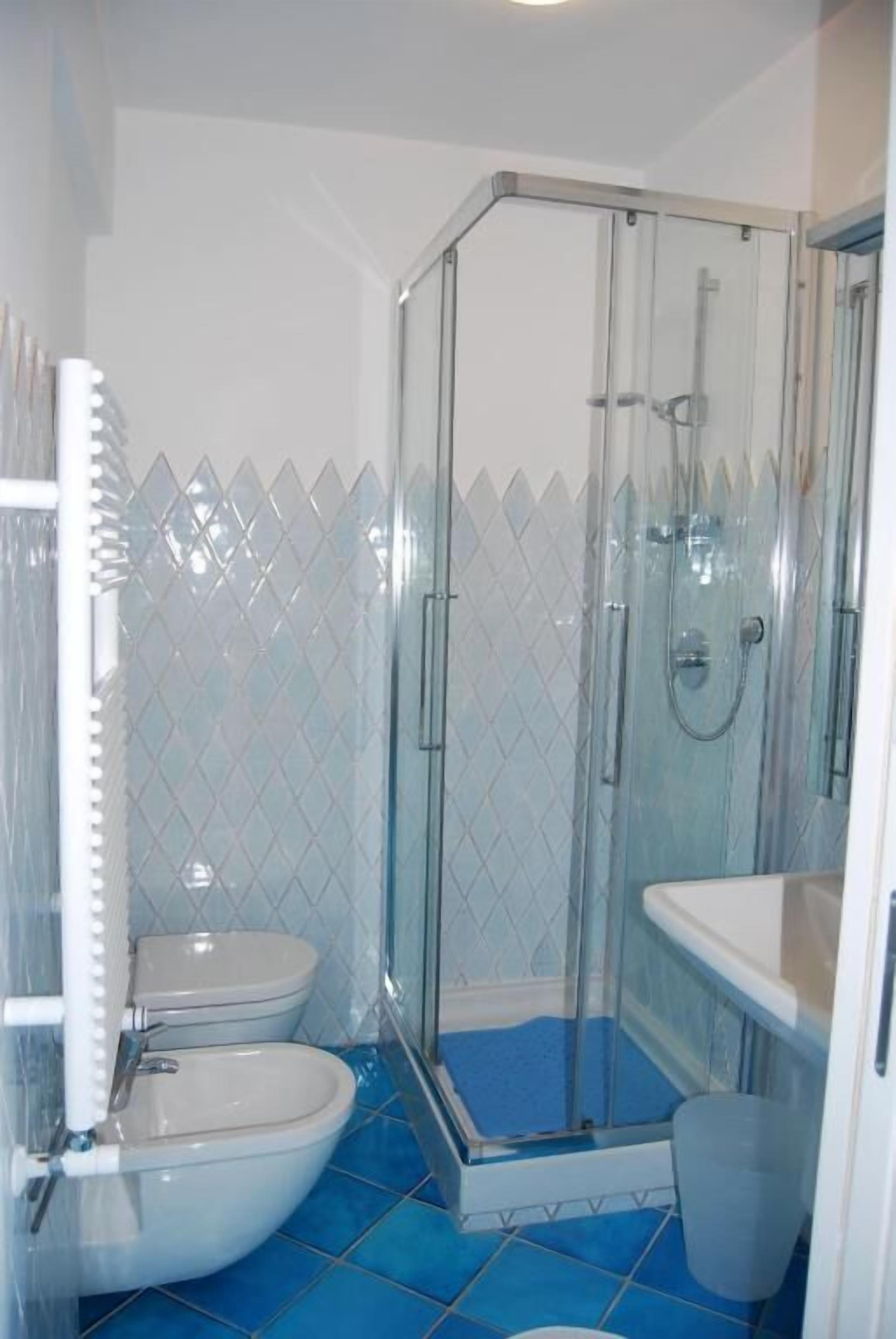 Un bany amb dutxa de vidre, dues vàteres i un lavabo.