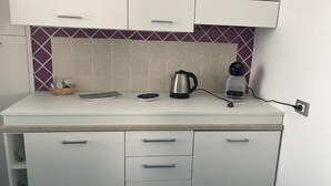 A kitchenette with a white countertop, a kettle, a coffee maker, and a basket with utensils. - Residenza Sveva (Ravello)