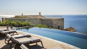A infinity pool with lounge chairs and a stone wall overlooking the sea. - Aria Estate (East Mani)