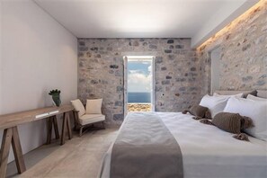 A bedroom with a stone wall, a bed, a desk, and a chair. - Aria Estate (East Mani)