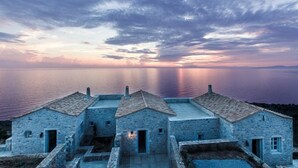 A coastal village with stone buildings, a calm sea, and a sunset sky. - Aria Estate (East Mani)