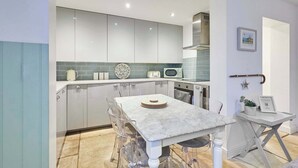 A modern kitchen with white cabinets, a marble countertop, and a clear glass table.