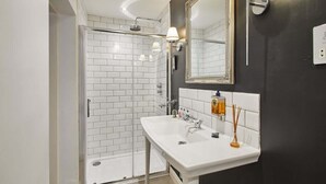 A modern bathroom with a white sink, a large mirror, and a glass-enclosed shower.