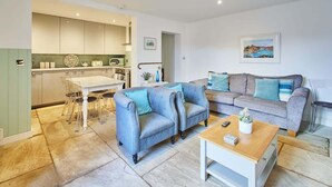A modern living room with a grey sofa, a wooden coffee table, and a dining area with a white table and chairs.