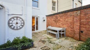 A courtyard with a white wall, a brick wall, a clock, and a table with chairs.