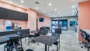 A modern kitchen area with dark cabinets, a coffee machine, and a seating area with tables and chairs. - Scottish Inns & Suites Houston, TX (Houston)