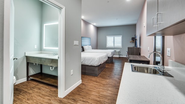 A modern bedroom with a large bed, a built-in desk, and a bathroom with a vanity. - Scottish Inns & Suites Houston, TX (Houston)