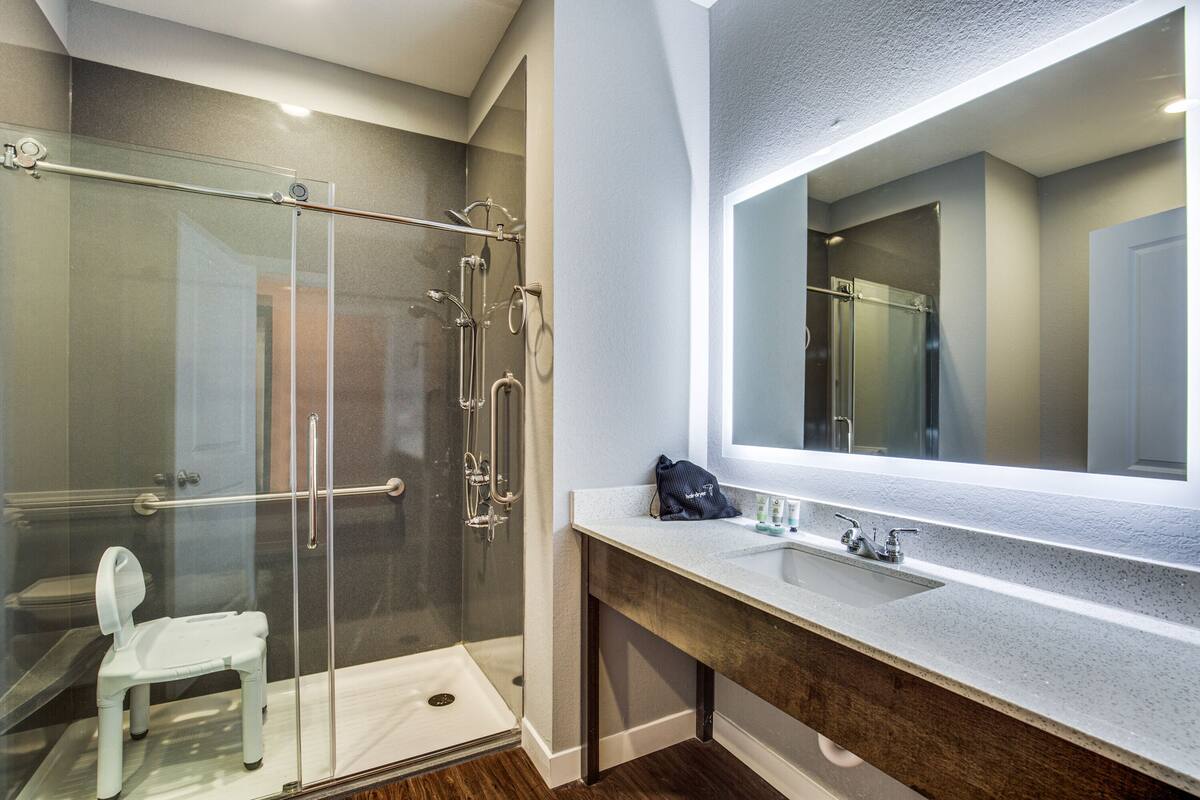 A modern bathroom with a glass shower enclosure, a white toilet, and a large mirror above a sink.