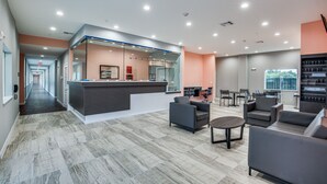 A modern lobby with a reception desk, seating area, and a staircase leading to other floors. - Scottish Inns & Suites Houston, TX (Houston)