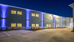 A modern building with a flat facade, multiple windows, and a well-lit entrance area. - Scottish Inns & Suites Houston, TX (Houston)