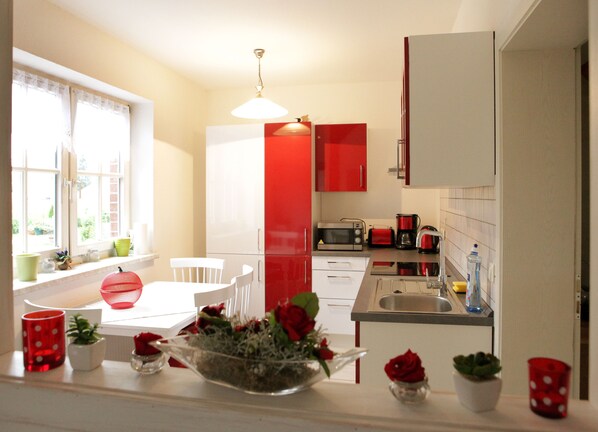 Una cocina moderna con armarios blancos y rojos, una mesa de comedor con sillas, un microondas, una cafetera y un lavamanos.