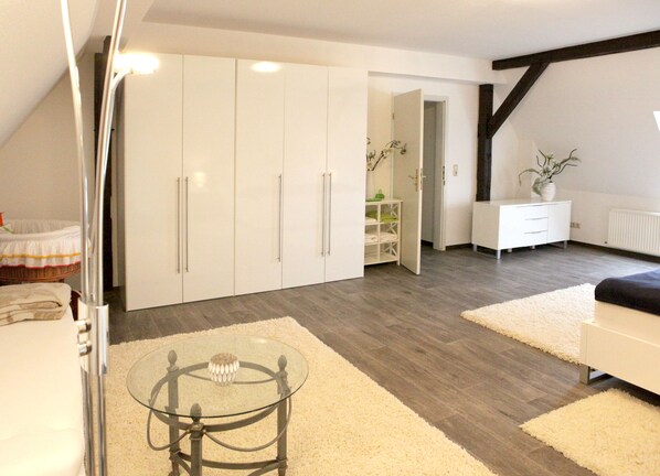 A modern bedroom with a glass table, white wardrobe, and a view of the living area.