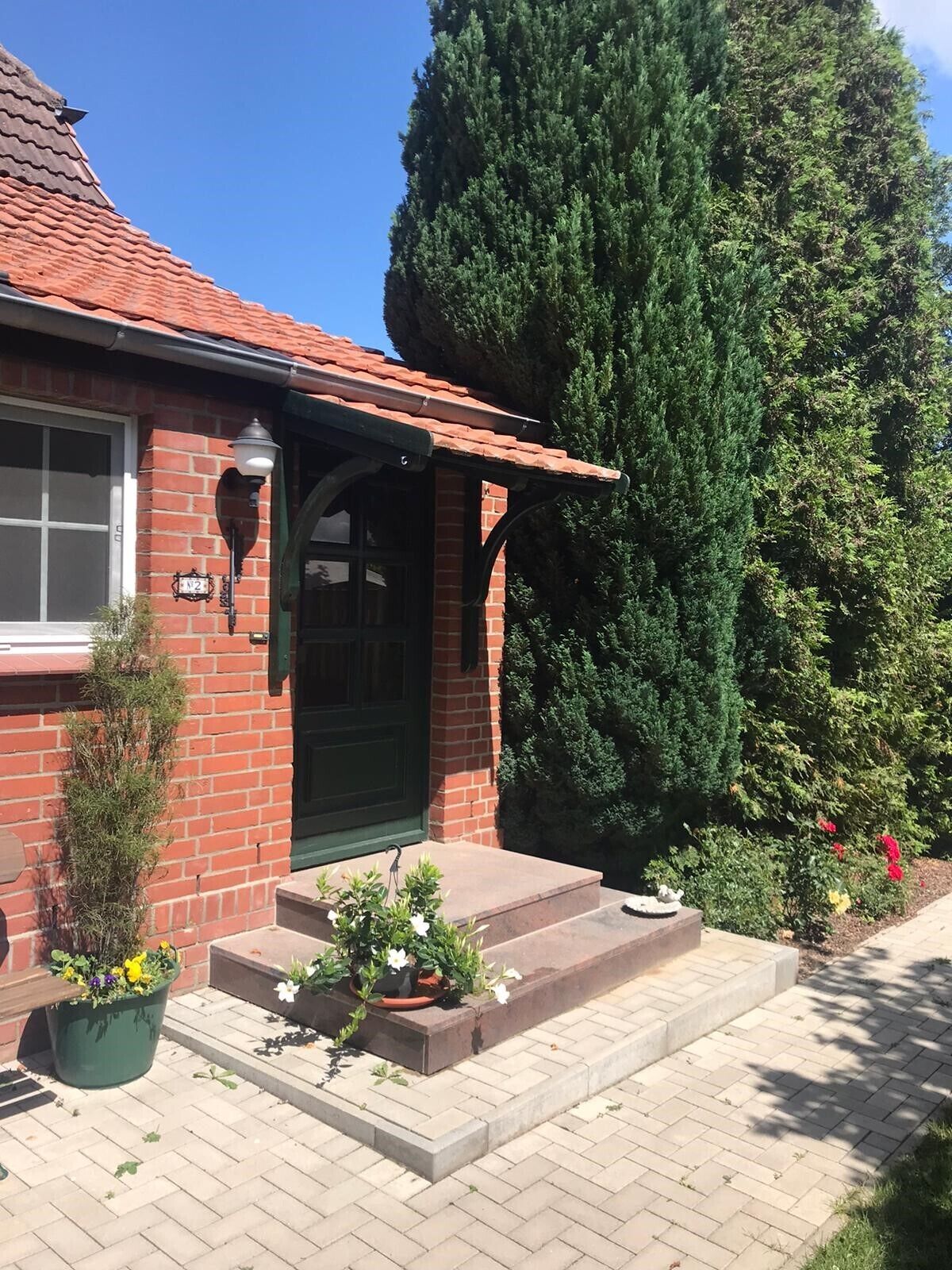 Una casa de maó amb una porta verda, un petit porxo i un gran arbre al davant.