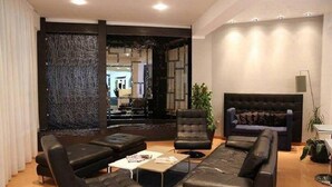 Uma sala de estar moderna com um sofá de couro preto, duas poltronas e uma mesa de centro. Há uma janela grande com cortinas, uma planta e um abajur.
