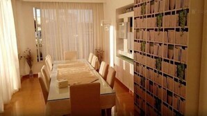 Uma sala de jantar com uma mesa comprida, cadeiras e uma estante com plantas em vasos.