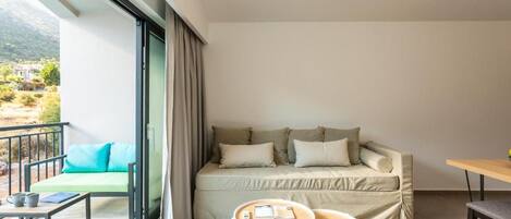 A modern room with a sofa, two small tables, a balcony with a view of greenery and mountains.