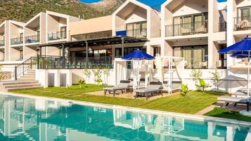 Un hotel con piscina, mobiliario exterior y montañas al fondo.