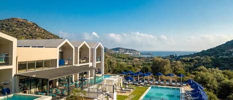 A hotel with multiple swimming pools, outdoor seating areas, and a view of the surrounding landscape.