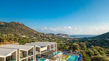 A hotel with a pool, multiple balconies, and a view of the sea and hills.