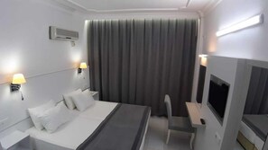 A hotel room with a bed, two bedside lamps, a flat-screen TV, a desk, and a large window with curtains. - Sunway Hotel (Alanya)