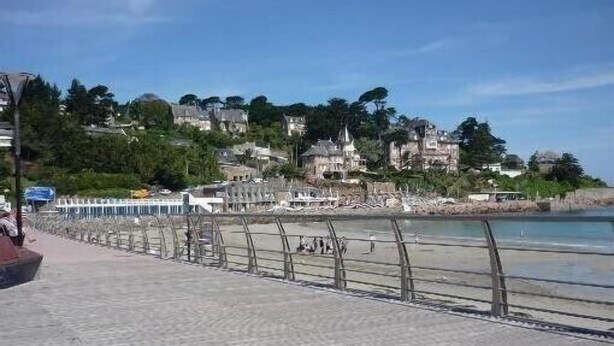 A coastal promenade with a paved walkway, a railing, and buildings in the background.