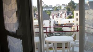 A balcony with a white table and chairs, overlooking a residential area with houses and a coffee shop.