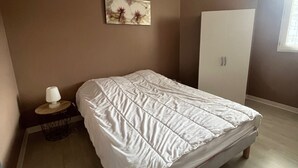 A bedroom with a bed, a nightstand, a lamp, a wardrobe, and a painting on the wall.