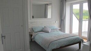 Quarto com uma cama, mesa de cabeceira, espelho e vista para o exterior através de uma porta de correr.