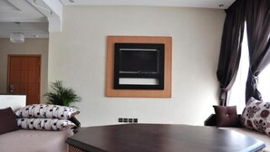 Una sala moderna con una amplia mesa de centro de madera oscura, un televisor de pantalla plana montado en la pared y un sofá con cojines estampados.
