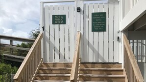 Una escalera de madera que conduce a un área con un muro, con dos letreros que indican acceso restringido y un aviso sobre la piscina.